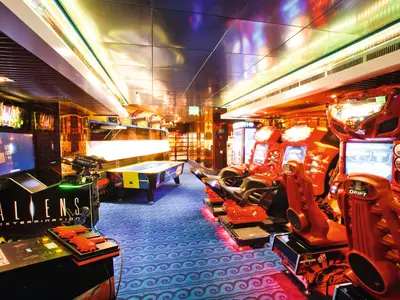 Eine beleuchtete Spielhalle an Bord der Costa Pacifica mit verschiedenen Arcade-Automaten, darunter Rennspiele und ein Schiessspiel im Vordergrund.