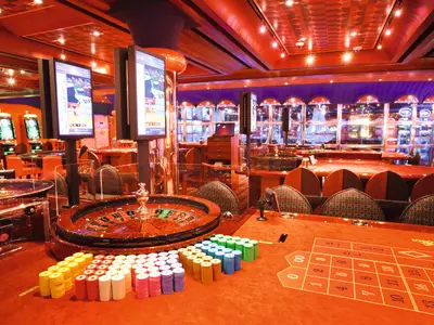 Blick auf den Roulettetisch mit bunten Jetons im Casinò Flamingo an Bord der Costa Pacifica, im Hintergrund Spielautomaten.