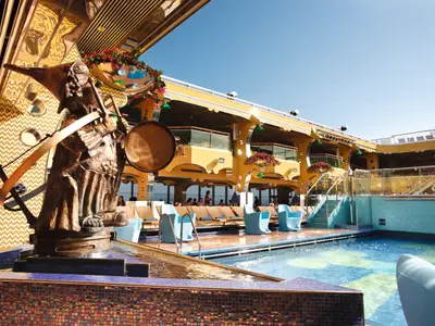 Der belebte Poolbereich Lido Calypso an Bord der Costa Pacifica zeigt eine große Skulptur und Liegestühle unter strahlend blauem Himmel.