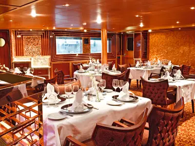 Elegantes Restaurant auf der Costa Pacifica. Festlich gedeckte Tische, Holzwände und gemütliche Stühle. Offene Küche im Hintergrund.