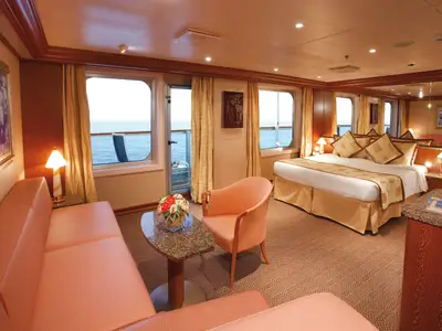 Innenansicht einer luxuriösen Suite an Bord der Costa Serena mit großem Doppelbett, Sitzecke und Aussicht auf das Meer.