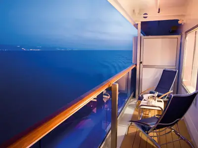 Balkon an Bord der Costa Serena mit zwei Liegestühlen, einem Beistelltisch und Blick auf das abendliche blaue Meer.