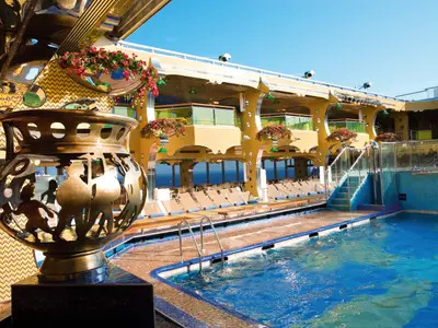 Der sonnige Poolbereich an Bord der Costa Serena mit einer goldenen Skulptur im Vordergrund, Liegestühlen und Meerblick.