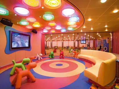 Bunter Squok Club Kinderbereich an Bord der Costa Serena mit farbenfrohen Hunden zum Sitzen, einem Sofa und leuchtenden Kreisen an der Decke.