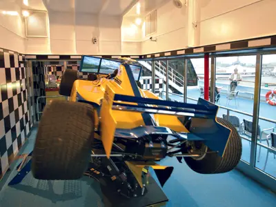 Der gelb-blaue Grand-Prix-Rennsimulator an Bord der Costa Serena steht in einem Raum mit schwarz-weiß karierten Wänden.