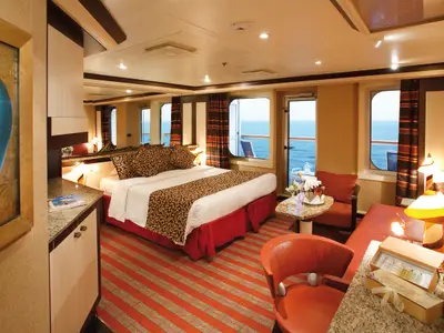 Blick in eine geräumige Samsara Suite an Bord der Costa Serena mit Doppelbett, Sitzecke und Balkon mit Meerblick.