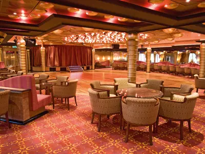 Grand Bar Apollo an Bord der Costa Serena mit goldenen Säulen, gemusterten Sesseln, runden Tischen und einer Tanzfläche im Hintergrund.