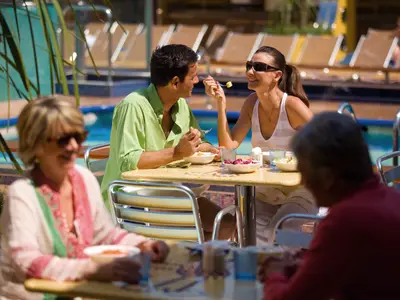 Ein lächelndes Paar beim Mittagessen am Außenpool an Bord der Costa Serena, im Hintergrund Sonnenliegen.