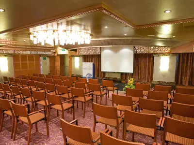 Einblick in den Konferenzraum an Bord der Costa Serena mit geordneten Stuhlreihen, Leinwand und moderner Deckenbeleuchtung.