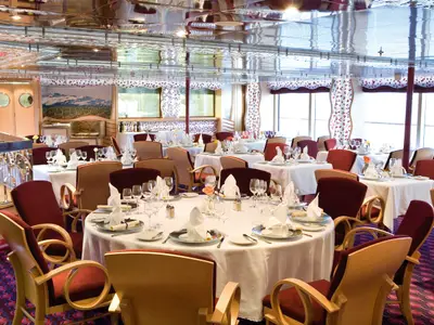 Eingedeckte Tische mit weißen Decken, Weingläsern, Servietten und roten Sesseln im Club-Restaurant Bacco an Bord der Costa Serena.