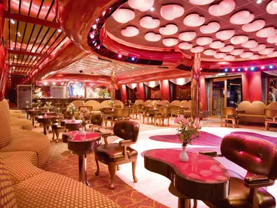Prunkvoller Cupido-Ballsaal an Bord der Costa Serena mit roten und goldenen Möbeln sowie herzförmigen Deckenleuchten.