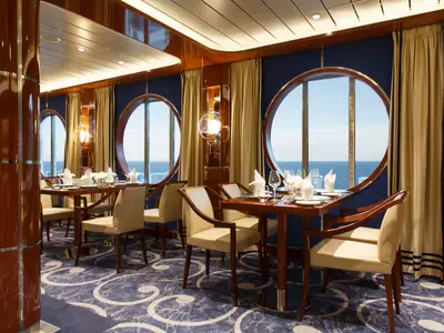 Gedeckte Tische und helle Sessel im eleganten Restaurant an Bord der Costa Smeralda mit Blick auf das blaue Meer.