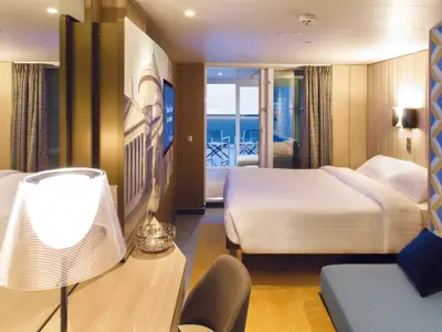 Eine moderne und gemütliche Balkonkabine an Bord der Costa Smeralda mit Doppelbett, Sitzbereich und Meerblick.