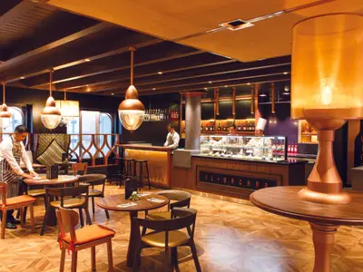 Gäste- und Barbereich des Restaurants Il Bacaro an Bord der Costa Smeralda mit Tischen aus Holz und warmen Lichtquellen.