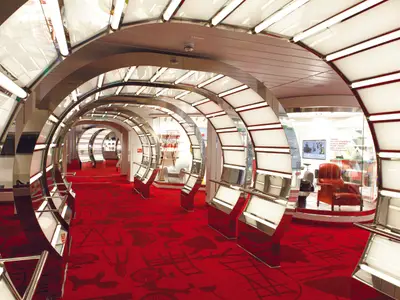 Ein Blick in das moderne Designmuseum CoDe an Bord der Costa Smeralda mit roten Teppichen und beleuchteten, geschwungenen Metallbögen.