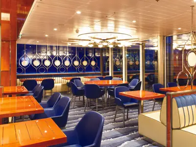 Ein schickes Restaurant an Bord der Costa Smeralda mit tiefblauen Sesseln, glänzenden Holztischen und einem modernen Lichtkonzept.