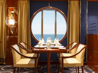 Ein elegant gedeckter Vierertisch mit Meerblick durch ein großes rundes Fenster an Bord der Costa Smeralda.