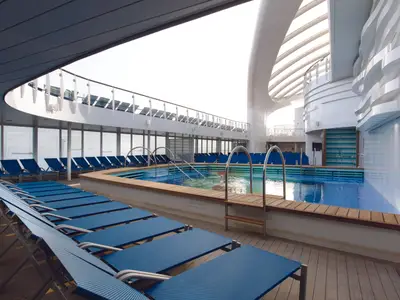 Der von blauen Liegestühlen umgebene Swimmingpool auf dem teilweise überdachten Deck der Costa Smeralda.