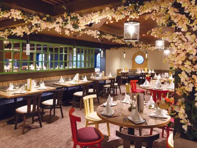 Das festlich dekorierte Rugantino-Restaurant an Bord der Costa Smeralda mit rosa Kunstblüten, Holztischen und bunten Stühlen.