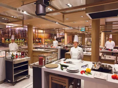 Köche stehen an modernen Kochstationen mit frischen Zutaten im Restaurant Laboratorio del Gusto an Bord der Costa Smeralda.