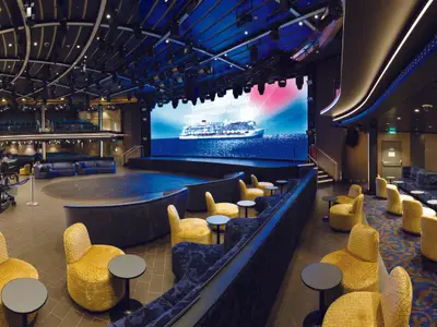 Blick in das moderne Teatro Sanremo an Bord der Costa Smeralda mit stilvollen gelben Sesseln und einer großen Bühne samt LED-Leinwand.