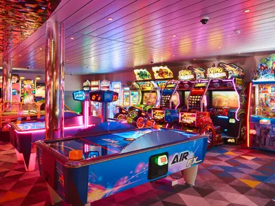 Blick in die neonbeleuchtete Arcade-Spielhalle an Bord der Costa Toscana mit Air-Hockey-Tischen und Fahrsimulatoren.