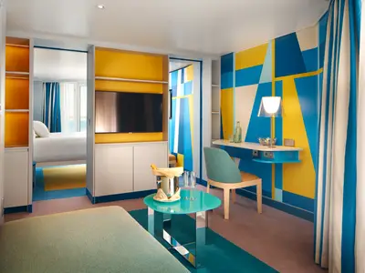 Wohnbereich einer modernen, bunt gestalteten Suite an Bord der Costa Toscana mit Schreibtisch und Blick ins Schlafzimmer.