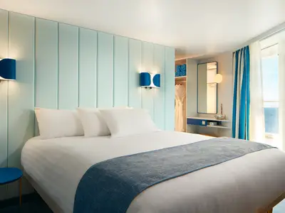 Modern eingerichtete Balkonkabine an Bord der Costa Toscana mit großem Bett, blau-weißer Wandgestaltung und Meerblick durch die Balkontür.