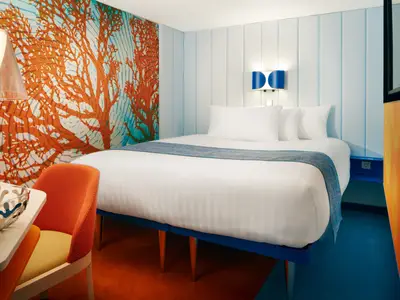 Gemütlich eingerichtete Innenkabine an Bord der Costa Toscana mit einem Doppelbett, einem orangefarbenen Stuhl und Kunst an der Wand.