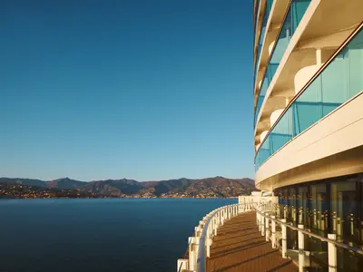 Die geschwungene Außenpromenade an Bord der Costa Toscana bietet einen weiten Blick auf das blaue Meer und die bergige Küste.