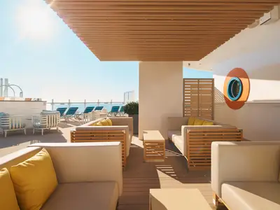 Gemütliche Lounge-Sessel mit gelben Kissen unter einer Holzüberdachung auf dem Sonnendeck an Bord der Costa Toscana.