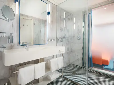 Ein luxuriöses, helles Badezimmer an Bord der Costa Toscana mit großem Waschbecken, Marmorwänden und einer Dampfdusche.
