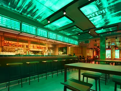 Die Heineken Star Club Bar an Bord der Costa Toscana zeigt eine moderne Einrichtung mit grünen Lichtinstallationen, Barhockern und Holztischen.