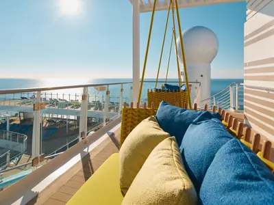 Bequeme Hängesofas mit gelben und blauen Kissen auf dem Außendeck an Bord der Costa Toscana mit weitem Meerblick.