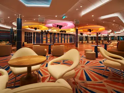 Moderne weiße Sessel, ein bunter Teppich und auffällige Deckenleuchten in der Gran Bar an Bord der Costa Toscana.