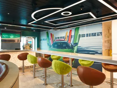 Moderne Sport-Bar an Bord der Costa Toscana mit grünen und braunen Barhockern und einer Wandgrafik von Sportwagen.