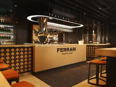 Die elegante Ferrari Bar 'Spazio Bollicine' an Bord der Costa Toscana mit einem Holztresen, Barhockern und Flaschendekor.