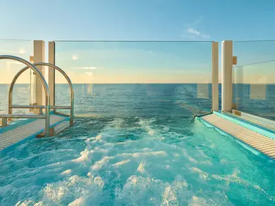 Ein sprudelnder Whirlpool mit einer Glaswand bietet an Bord der Costa Toscana einen ungestörten Blick auf das weite Meer bei Sonnenuntergang.