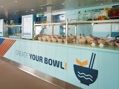 Die Kiki Poke Station an Bord der Costa Toscana zeigt eine Theke mit der Aufschrift 'Create Your Bowl' und frischen Zutaten.
