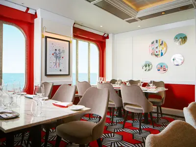 Eingedeckte Tische und weiche Samtsessel im stilvollen Restaurant L'Argentario an Bord der Costa Toscana mit Blick auf das Meer.