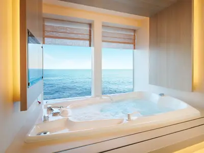 Ein luxuriöser Whirlpool mit schäumendem Wasser direkt vor großen Fenstern mit Blick auf das weite blaue Meer an Bord der Costa Toscana.