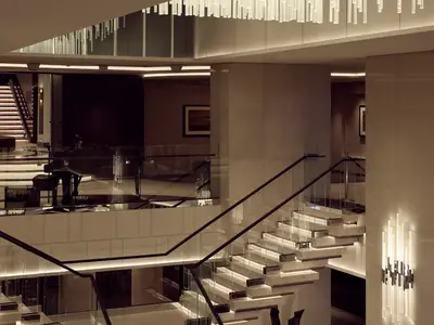 Das moderne Atrium an Bord der Explora I zeigt eine beleuchtete Treppe mit Glaselementen, warmes Licht und ein Klavier im Obergeschoss.
