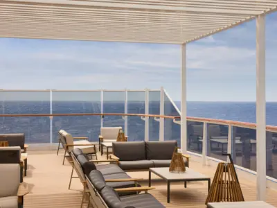 Überdachte Außenlounge mit bequemen Sofas, Holztischen und Glasreling mit freiem Blick auf das Meer an Bord der Explora I.