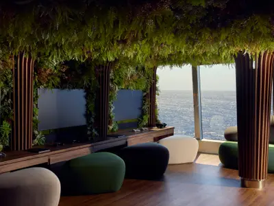 Der gemütliche Nautilus Club an Bord der Explora I mit begrünten Wänden, Sitzkissen, Bildschirmen und Blick aufs Meer.