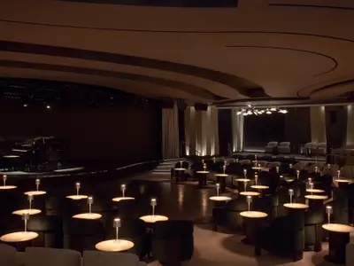 Der elegant abgedunkelte Show-Saal an Bord der Explora I mit erleuchteten Tischlampen und einem Flügel auf der Bühne.