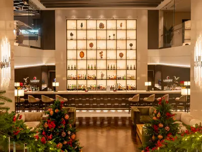 Elegante Lobby Bar an Bord der Explora I mit einer beleuchteten Regalwand, Barhockern und festlichen Weihnachtsbäumen im Vordergrund.