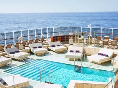 Der Atoll Pool an Bord der Explora I mit flachem Wasser, gemütlichen Doppel-Sonnenliegen und freiem Blick auf das Meer.