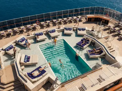 Blick von oben auf das elegante Pooldeck an Bord der Explora I mit türkisfarbenem Pool, Sonnenliegen und Meerblick.