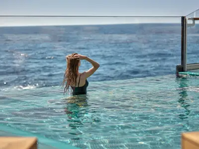 Eine Frau blickt im beheizten Infinity-Pool an Bord der Explora I auf den weitläufigen blauen Ozean.