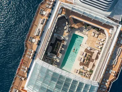 Blick aus der Vogelperspektive auf den Pool und das elegante Sonnendeck an Bord der Explora I direkt am Meer.